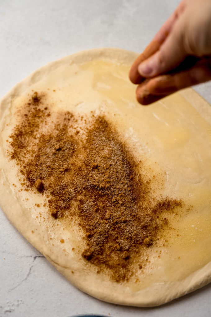 Someone is sprinkling cinnamon sugar on a rectangle of dough to make sticky buns.