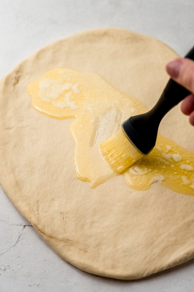 Someone is brushing melted butter onto a rectangle of dough to make sticky buns.