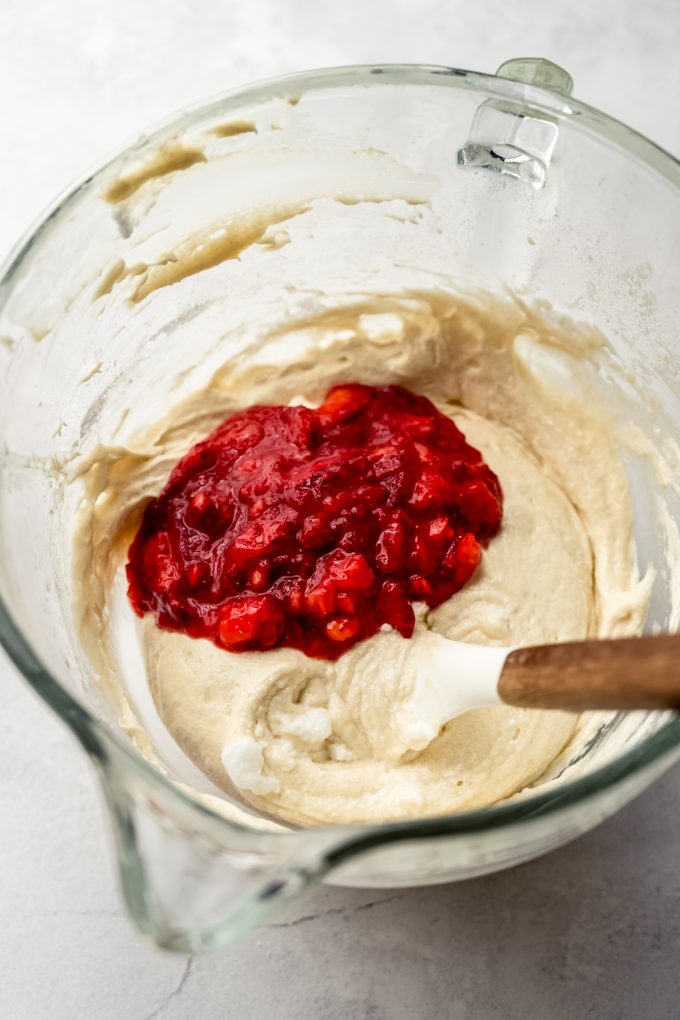 Strawberry cupcake batter in a bowl with a spatula ready to mix in the strawberries.