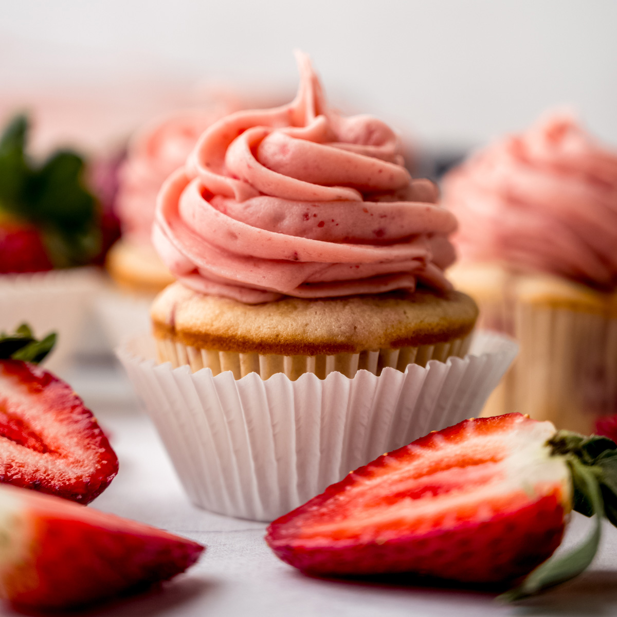 A frosted strawberry cupcake on a surface.