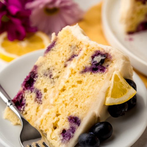 A slice of lemon blueberry cake on a plate with a fork.