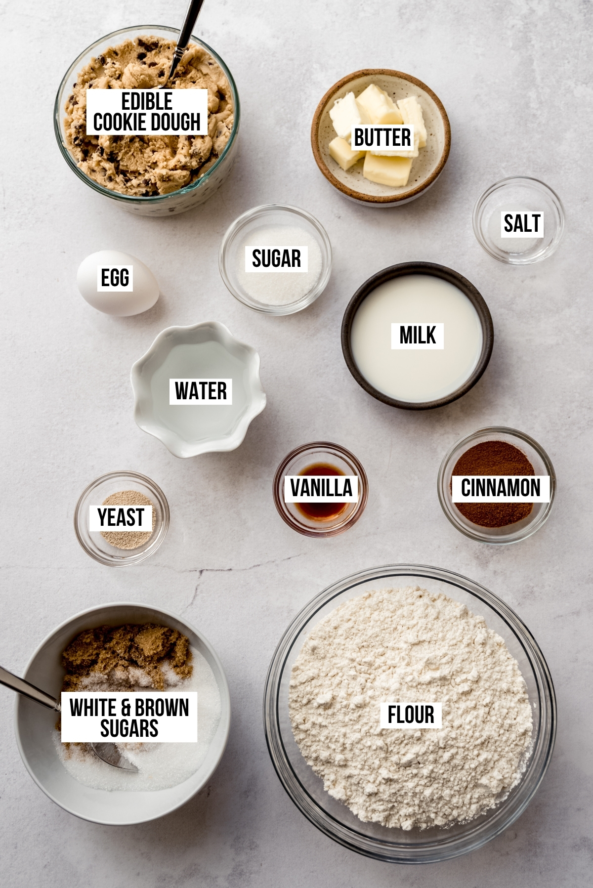 Aerial photo of ingredients to make cookie dough cinnamon rolls with text overlay labeling each ingredient.