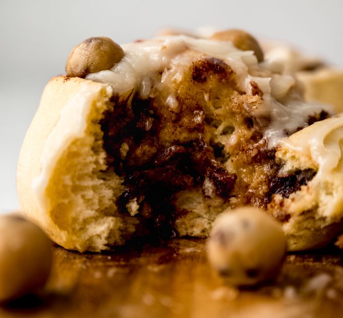 A cookie dough cinnamon roll on a surface and it has a bite taken out of it so you can see the inside of the roll.