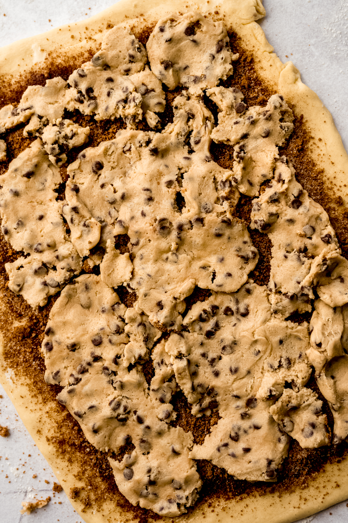 Aerial photo of a rectangle of dough for cookie dough cinnamon rolls with filling and cookie dough scattered all over it.