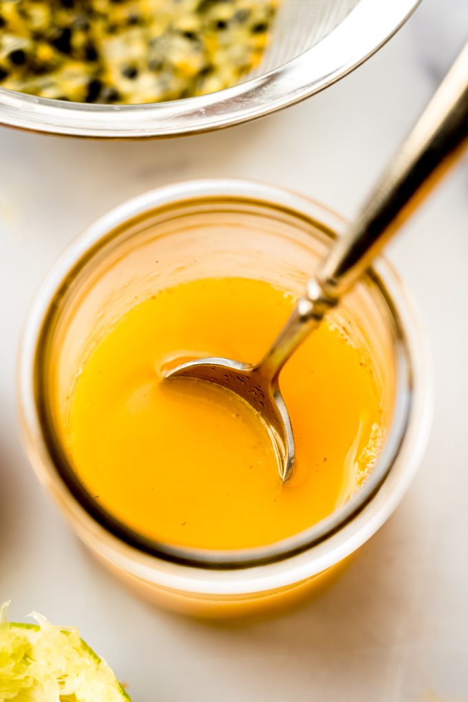 Passion fruit dressing in a small glass container with a spoon.
