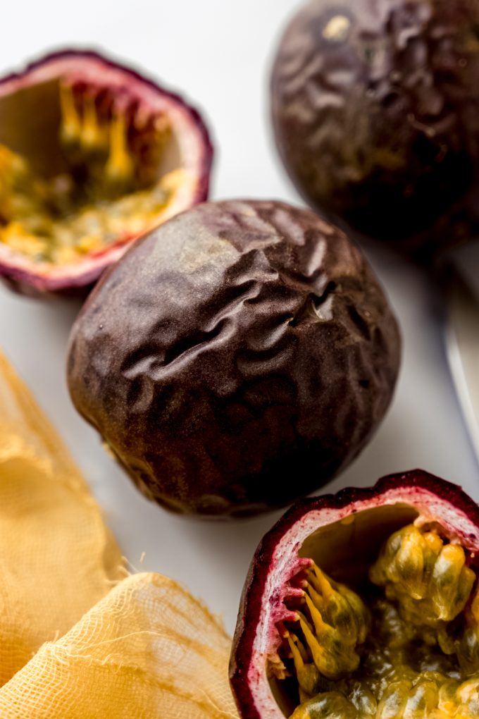 Whole and halved passion fruits on a surface.
