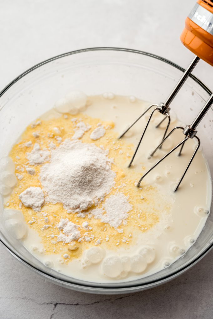 A large glass bowl with pudding mix and milk ready to get mixed together with an electric mixer.