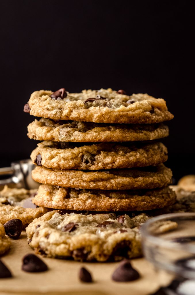 A stack of brown butter chocolate chip cookies on parchment paper with chocolate chips in the foreground.