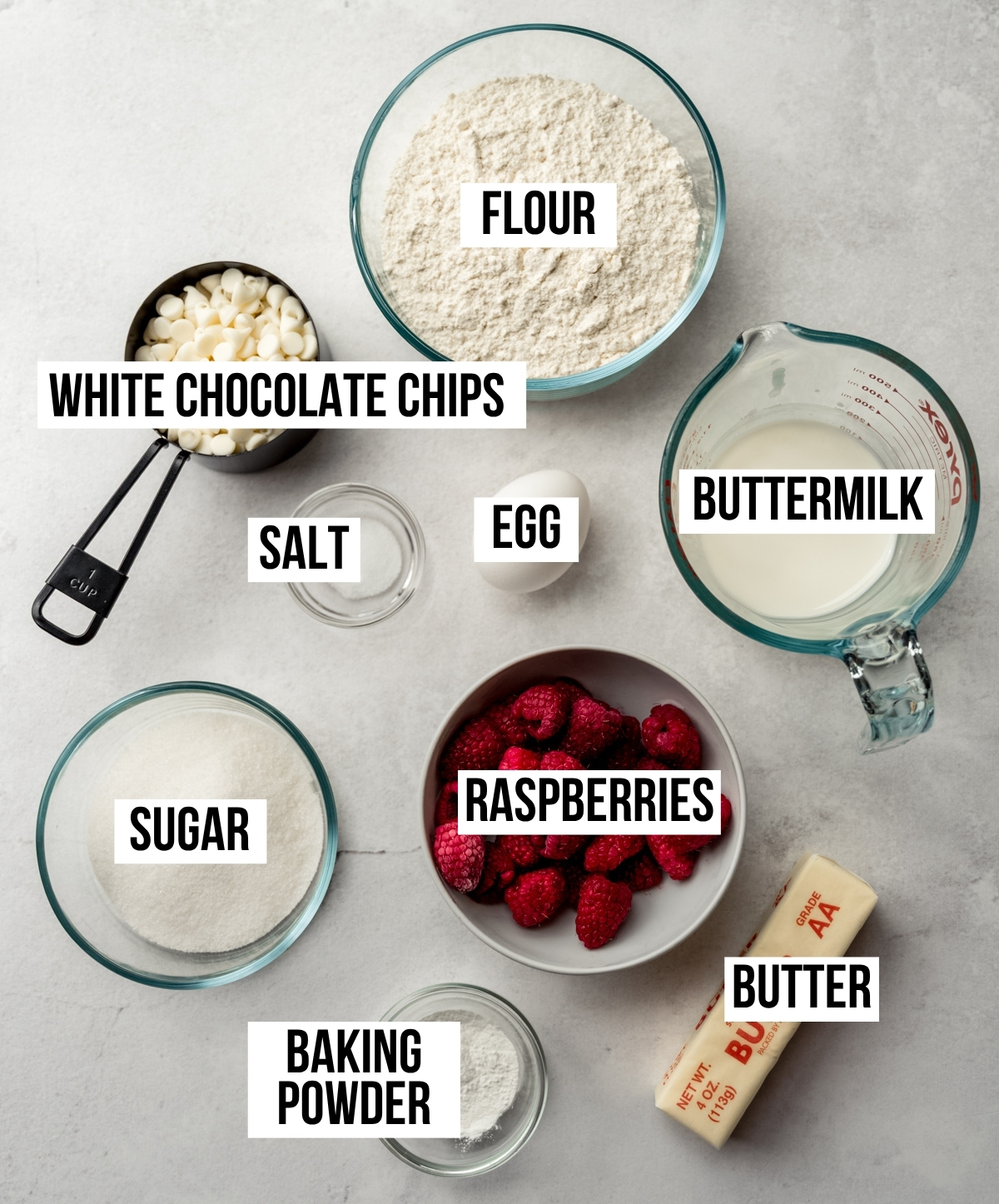 Aerial photo of ingredients to make raspberry white chocolate chip scones with text overlay labeling each ingredient.