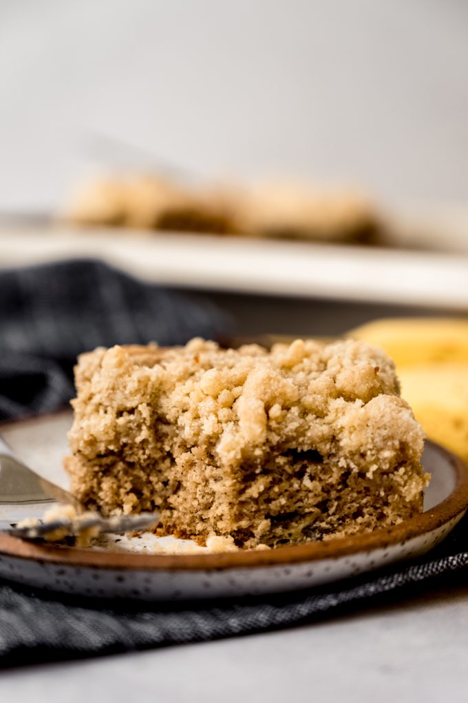 A slice of banana crumb cake on a plate with a fork and a bite taken out of the cake.