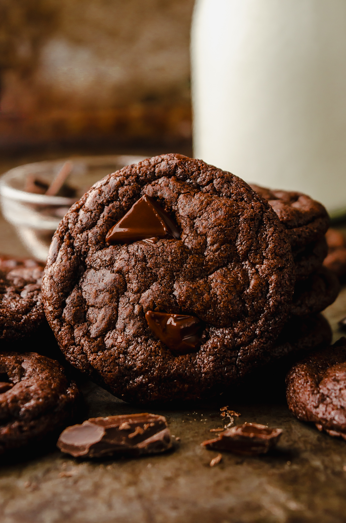 Dark chocolate cookies on a surface with a jug of milk in the background.