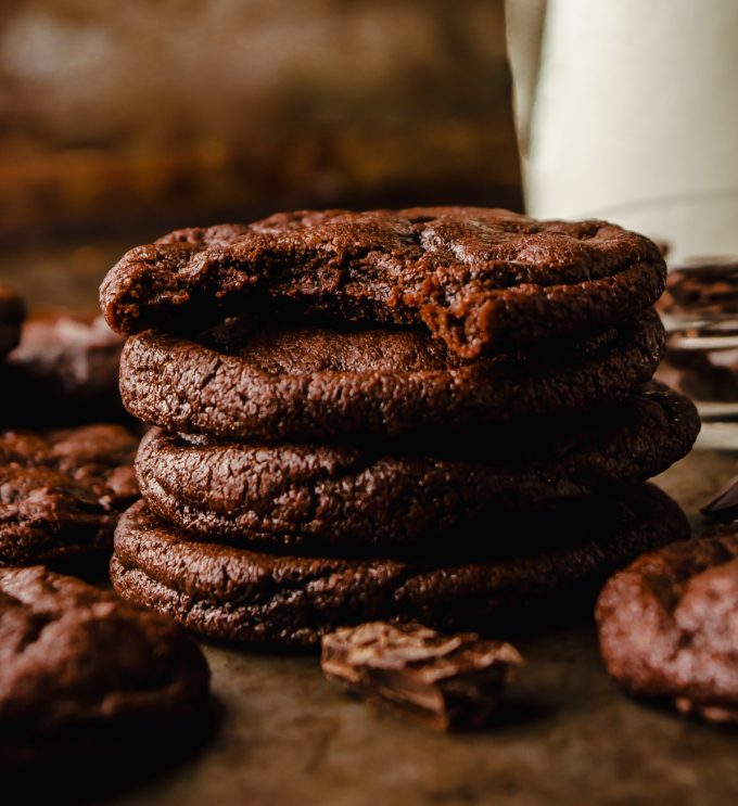 A stack of dark chocolate cookies on a surface and a bite has been taken out of the one on the top.