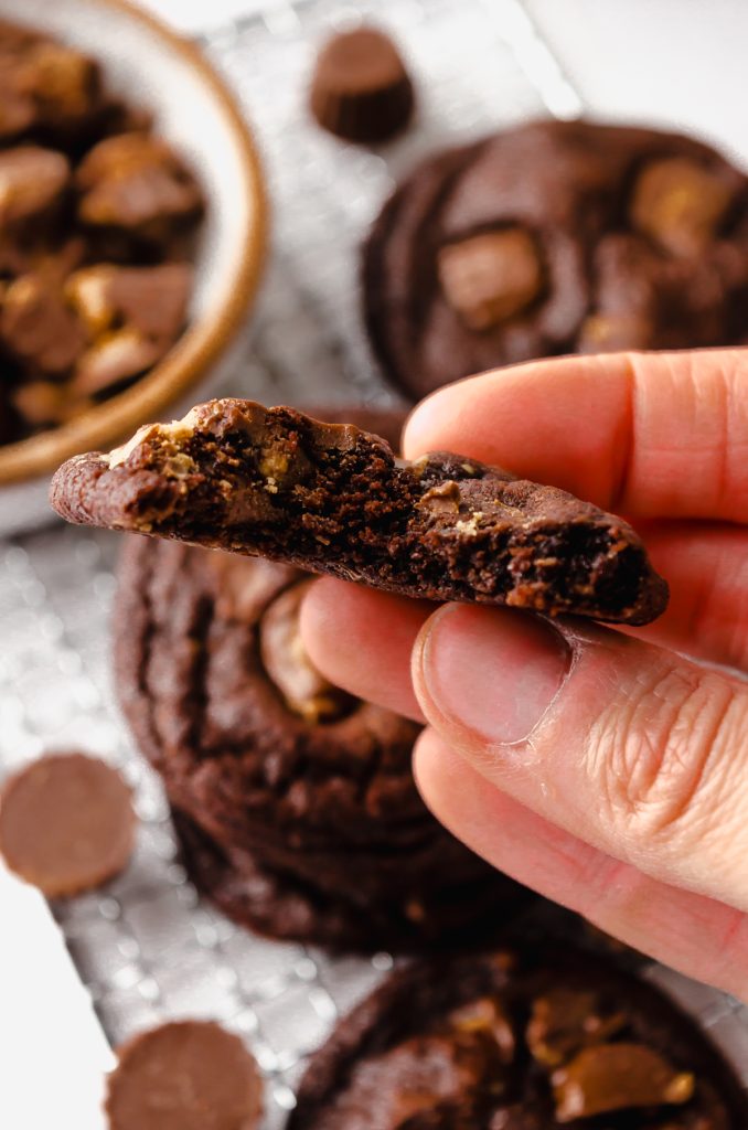 Someone is holding one half of a chocolate peanut butter cup cookie that has been bitten into.