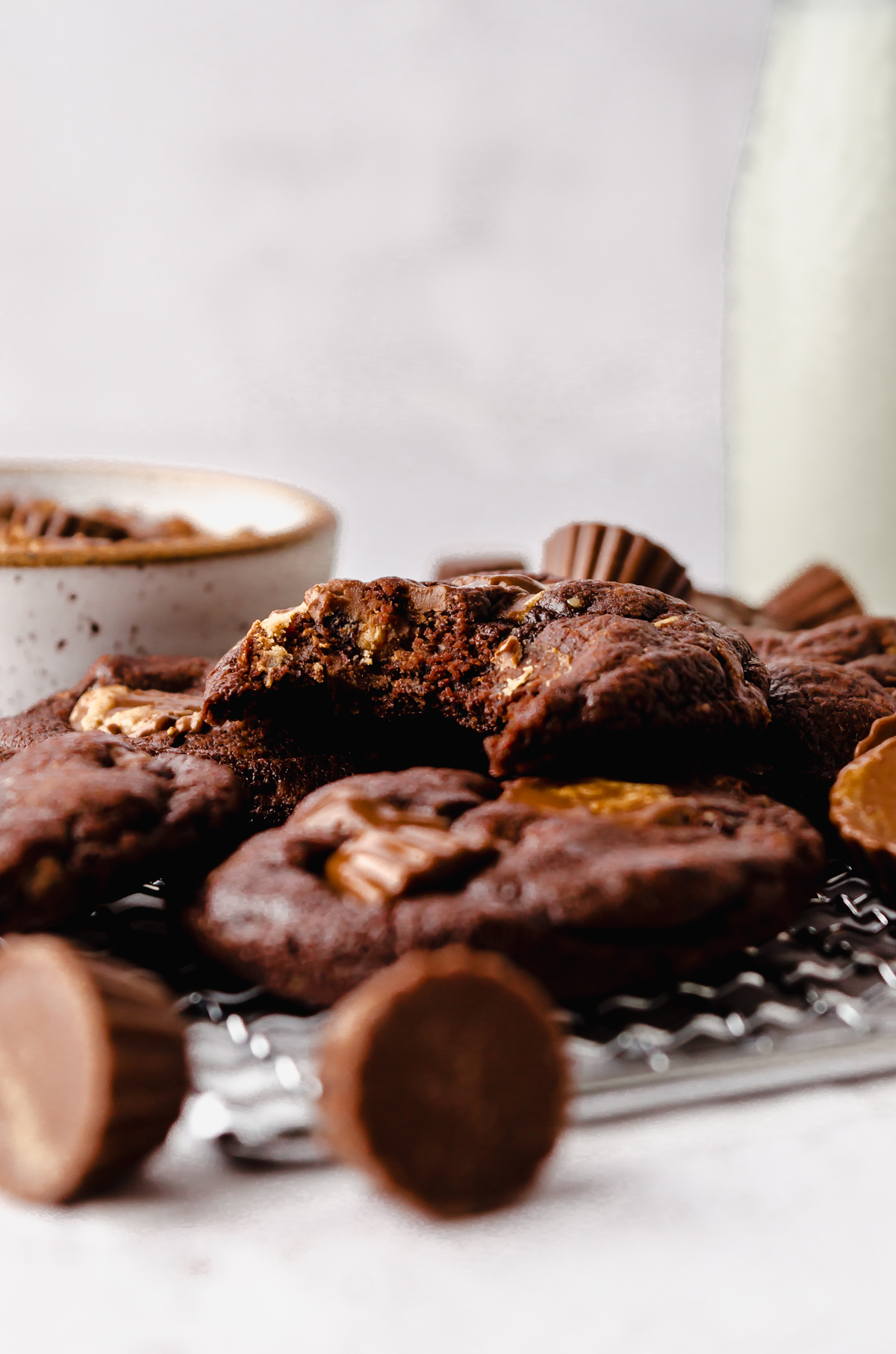 A photo of a chocolate peanut butter cup cookie with a bite taken out of it on a surface with peanut butter cups around it.