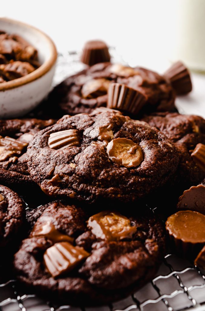 A photo of a chocolate peanut butter cup cookie on a surface with peanut butter cups around it.