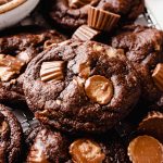 A photo of a chocolate peanut butter cup cookie on a surface with peanut butter cups around it.