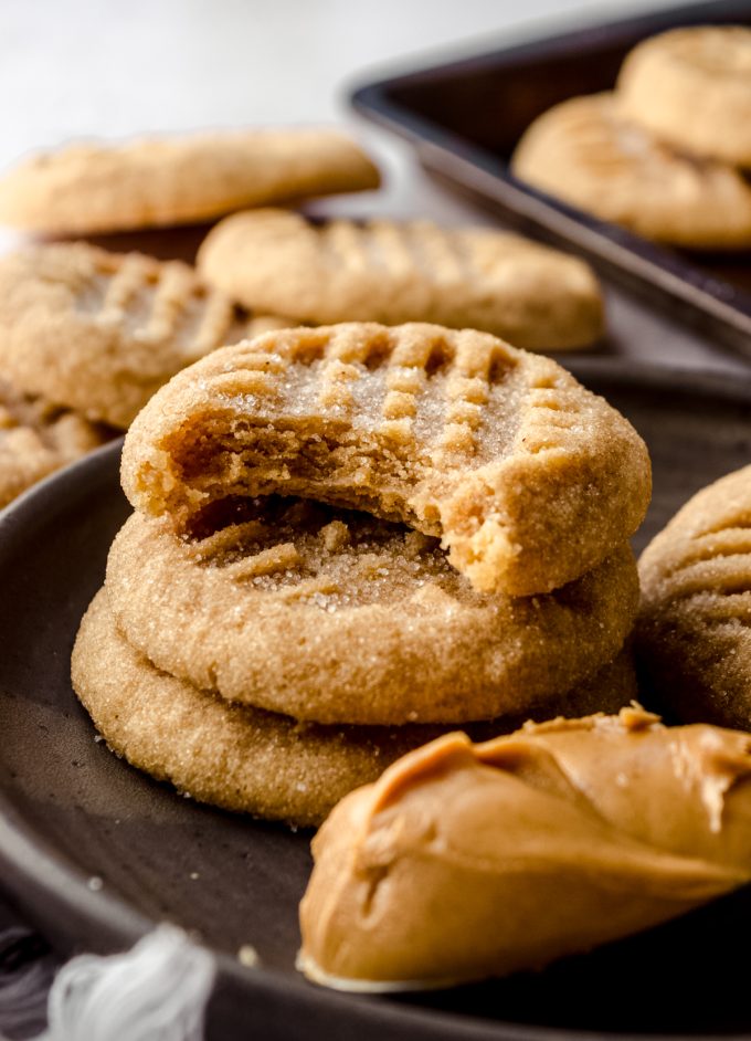 A stack of classic peanut butter cookies on a plate and a bite has been taken out of the one on the top.