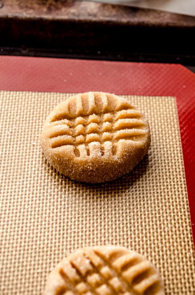 Classic peanut butter cookie dough ball that has been imprinted with a criss-cross pattern and is ready to bake.