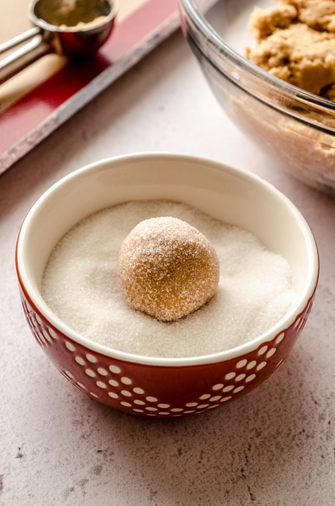 A peanut butter cookie dough ball in a bowl of sugar.