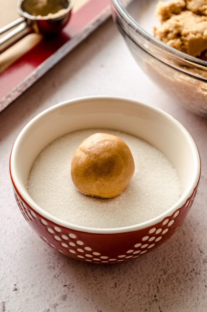 A peanut butter cookie dough ball in a bowl of sugar.