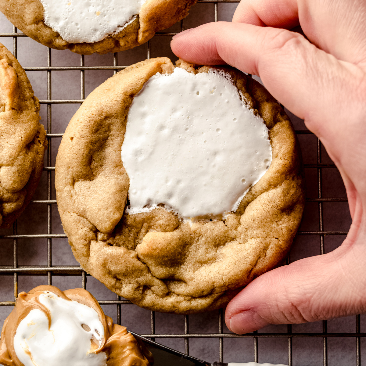 Someone is picking up a fluffernutter cookie from a cooling rack.