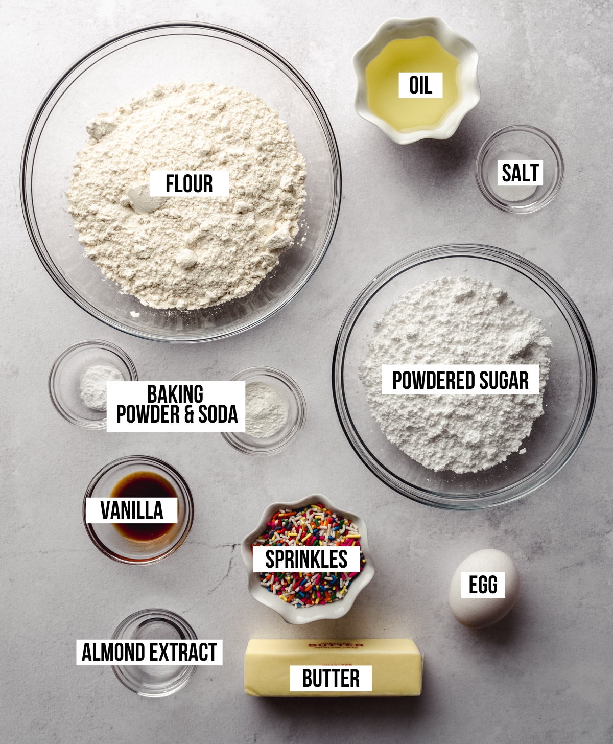 Aerial photo of ingredients to make funfetti sugar cookies with text overlay labeling each ingredient.