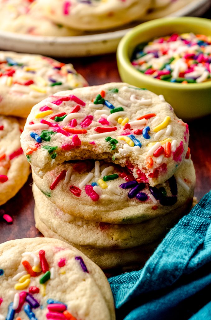 A stack of funfetti sugar cookies and a bite has been taken out of the one on the top.