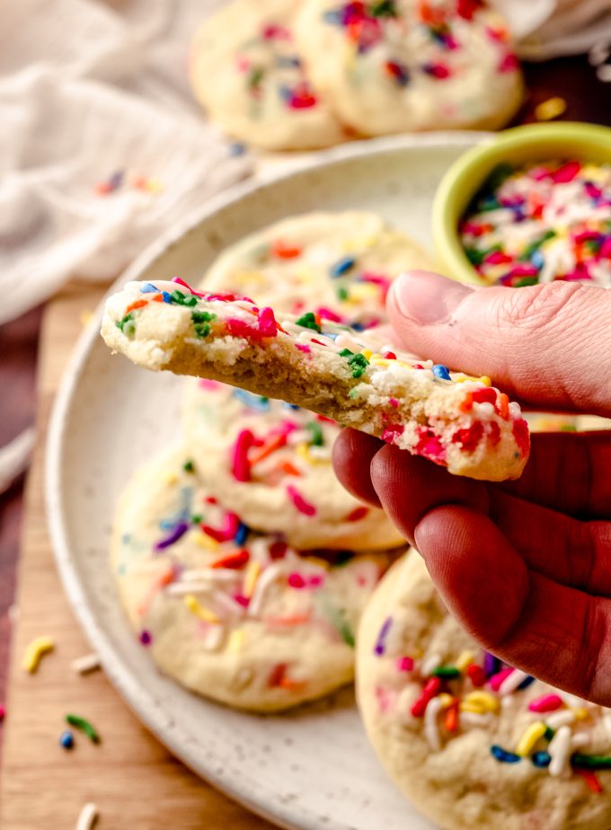 Someone is holding a funfetti sugar cookie with a bite taken out of it.