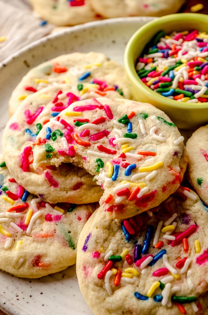 A plate of funfetti sprinkle sugar cookies with a bite taken out of the one on the top.