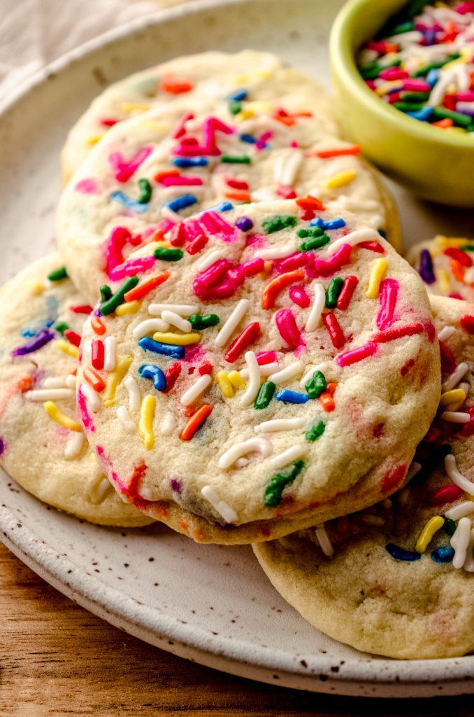 A plate of funfetti sprinkle sugar cookies with a small bowl of sprinkles in the background.