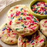 A plate of funfetti sprinkle sugar cookies with a small bowl of sprinkles.