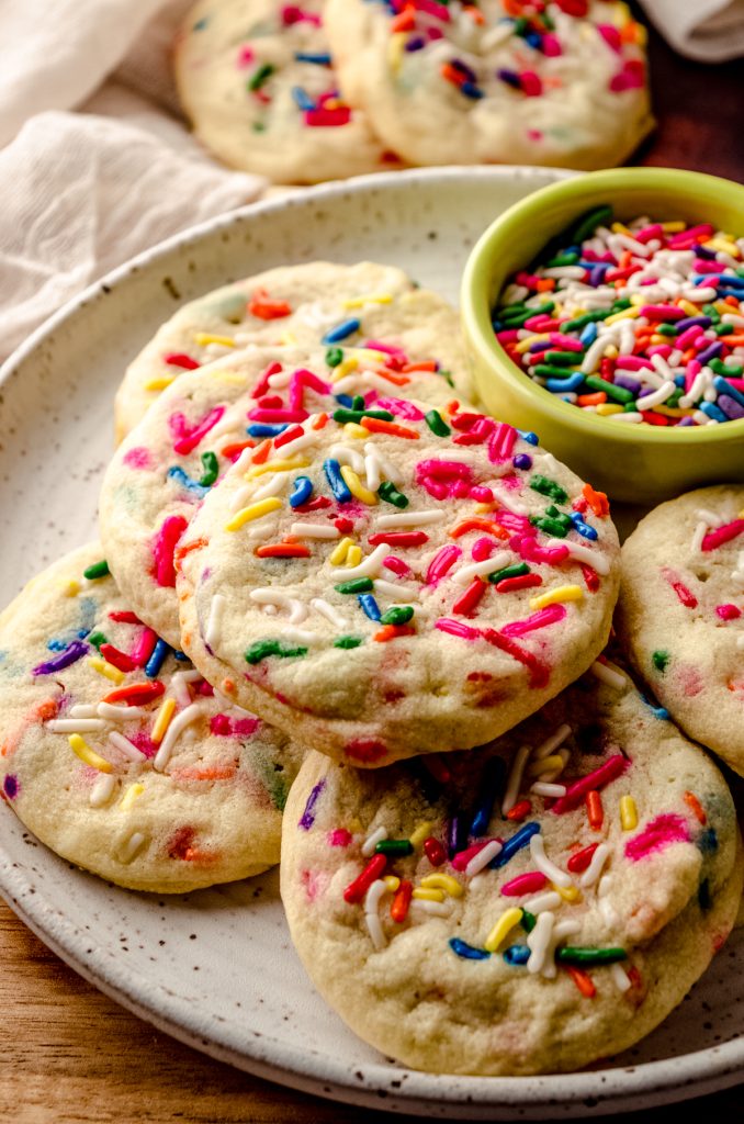 A plate of funfetti sprinkle sugar cookies with a small bowl of sprinkles.