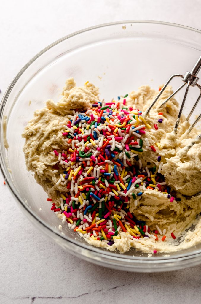 A bowl of funfetti sugar cookie dough with electric beaters in it.