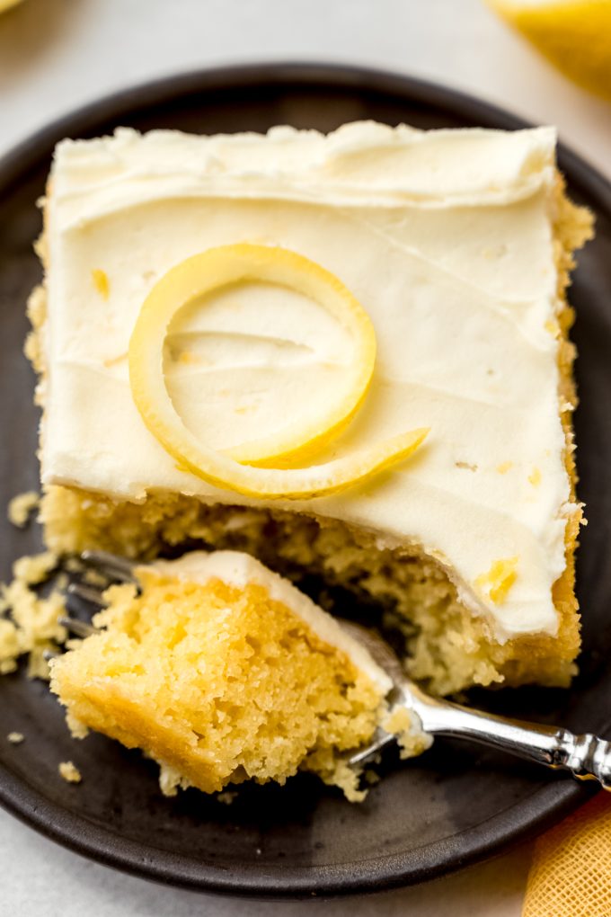 A slice of lemon sheet cake with a bite taken out of it with a fork.