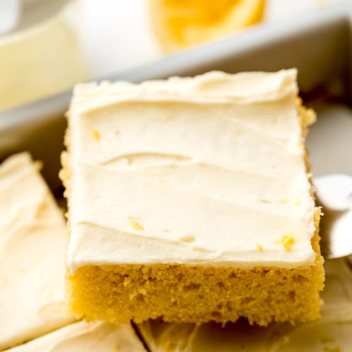 Someone is using a spatula to lift a slice of lemon sheet cake out of a baking pan.