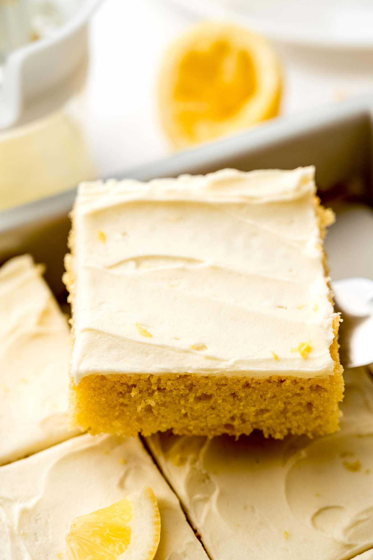 Someone is using a spatula to lift a slice of lemon sheet cake out of a baking pan.