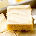 Someone is using a spatula to lift a slice of lemon sheet cake out of a baking pan.