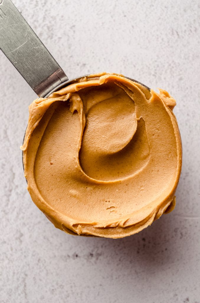 A measuring cup full of creamy peanut butter. 