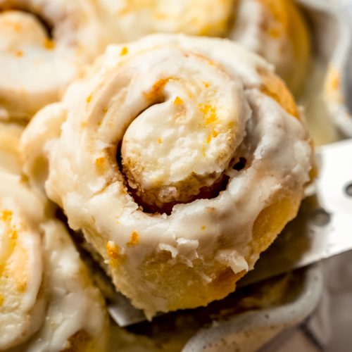 Someone is lifting an orange cinnamon roll out of a dish of baked rolls.