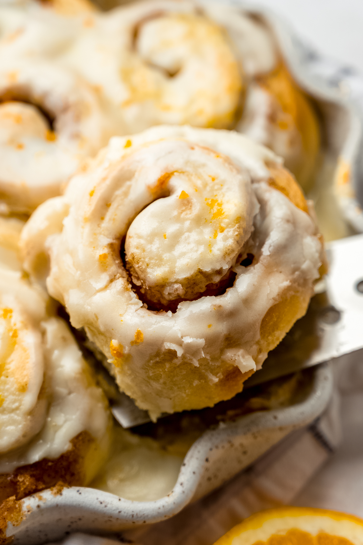 Someone is lifting an orange cinnamon roll out of a dish of baked rolls.