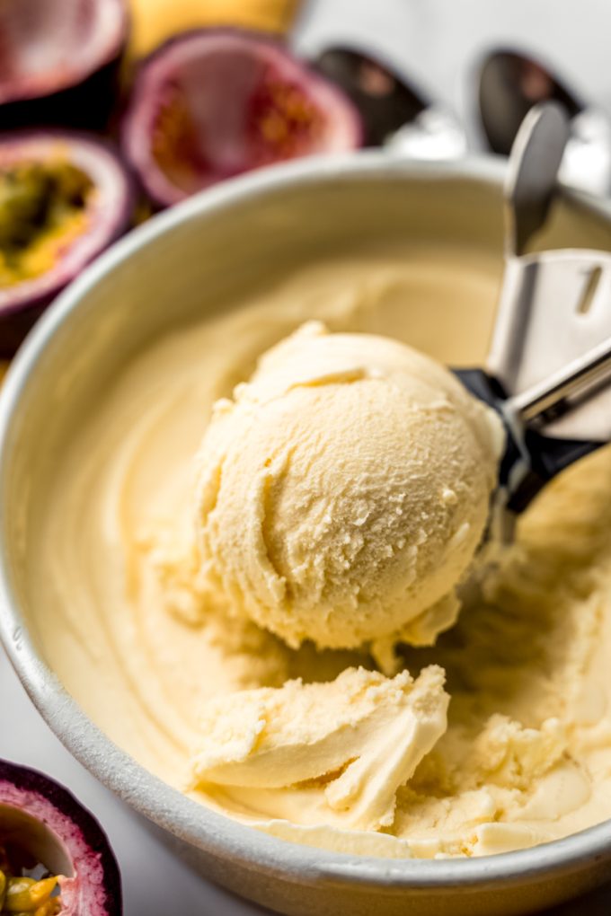 Passion fruit ice cream in a container getting scooped out with an ice cream scoop.