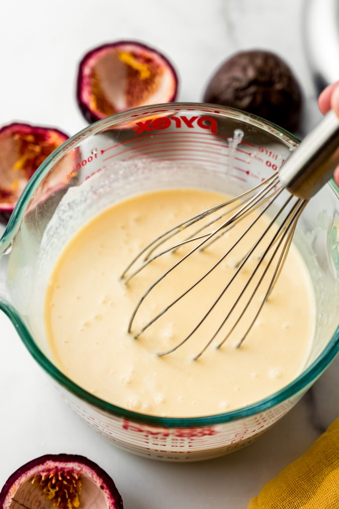 A glass measuring cup full of passion fruit ice cream mix with a whisk in it.