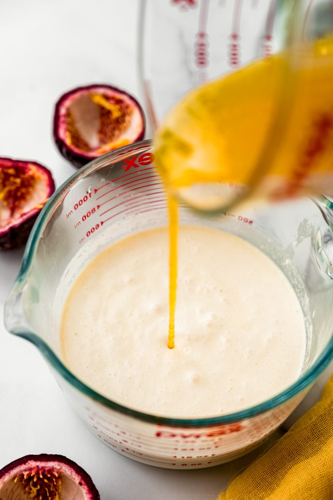 Someone is pouring passion fruit reduction into a measuring cup of cream and milk to make ice cream.