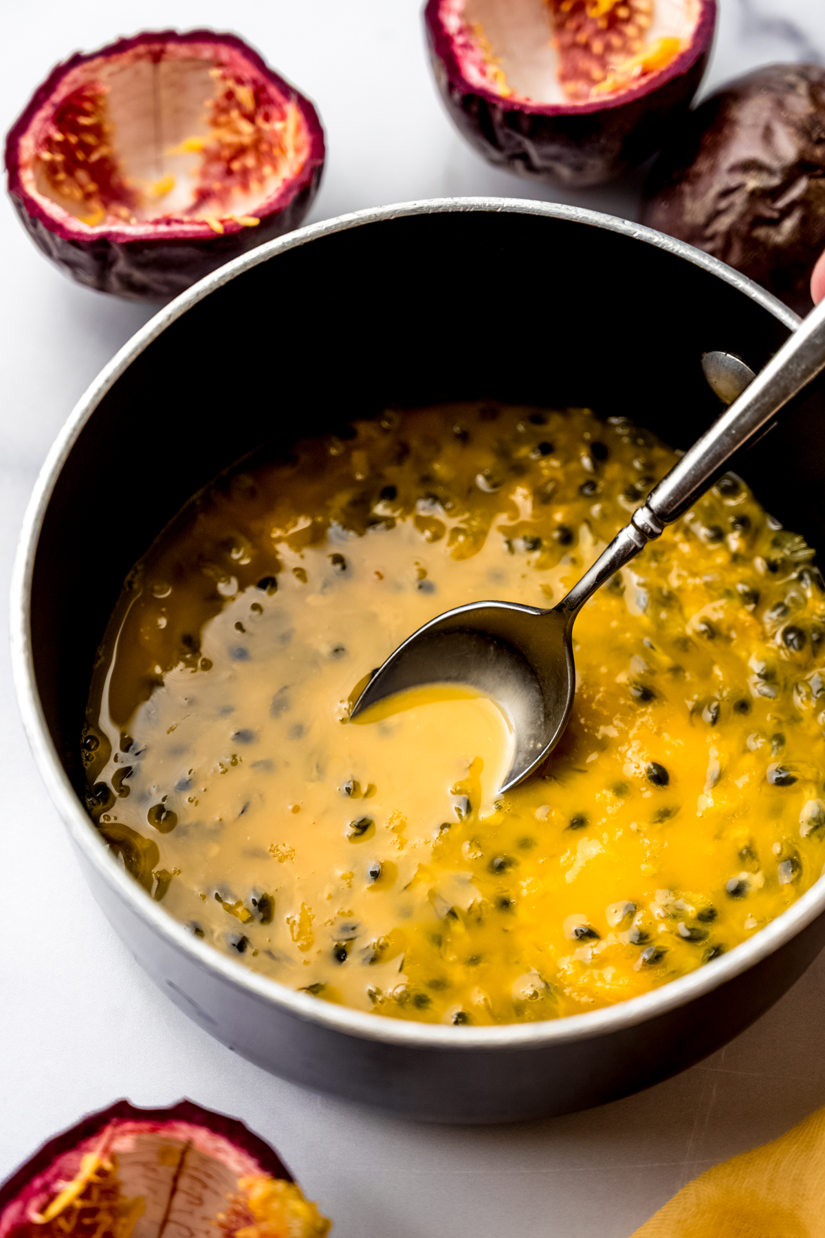 A saucepan with passion fruit pulp and seeds and a spoon in it.