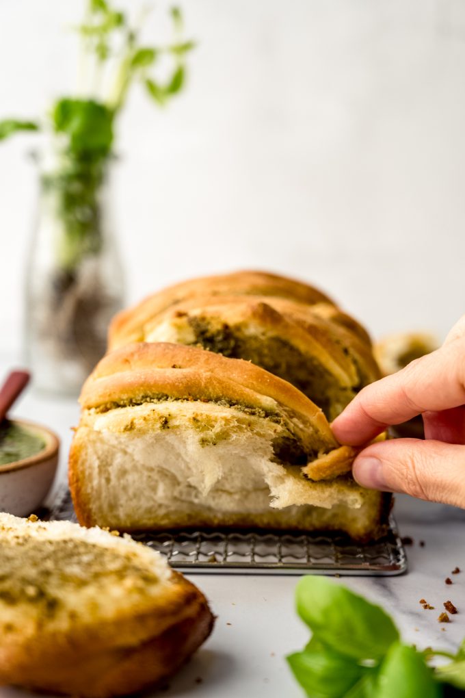 Someone is pulling apart a loaf of pesto pull-apart bread that is sitting on a surface.