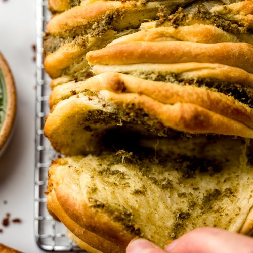 Aerial photo of pesto pull-apart bread that someone is pulling apart.