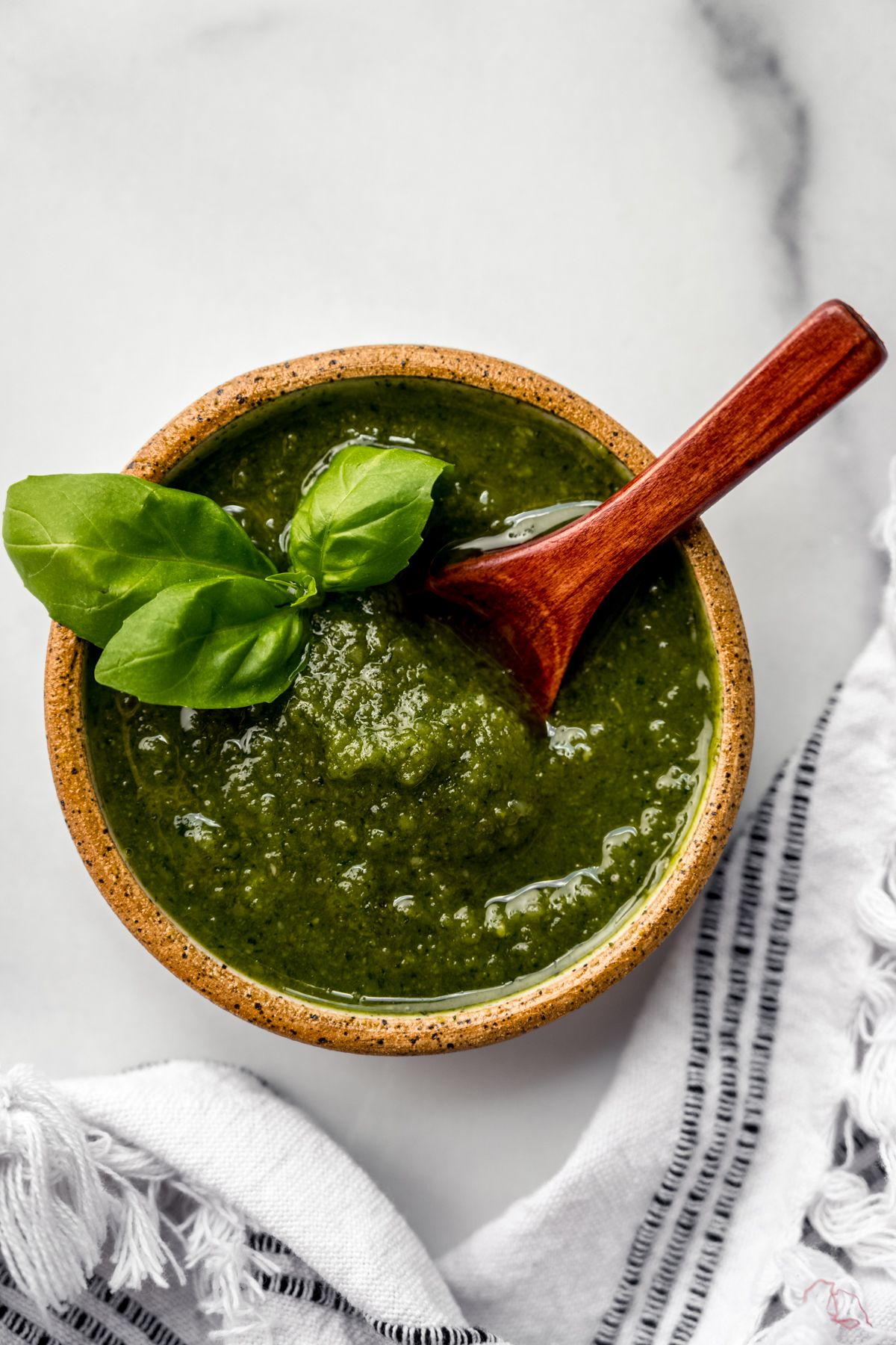 A bowl of homemade pesto with a small wooden spoon in it.