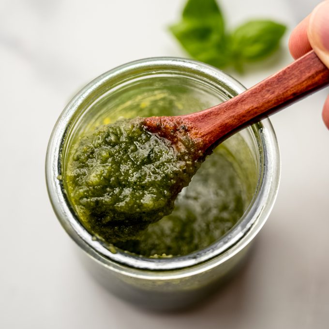 A jar of homemade pesto with a small wooden spoon in it.