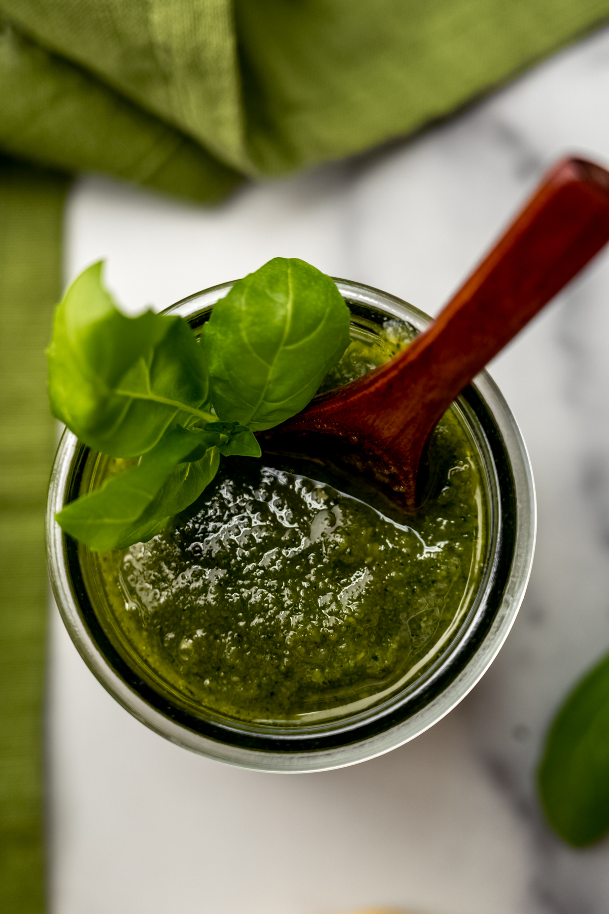 A jar of homemade pesto with a small wooden spoon in it.
