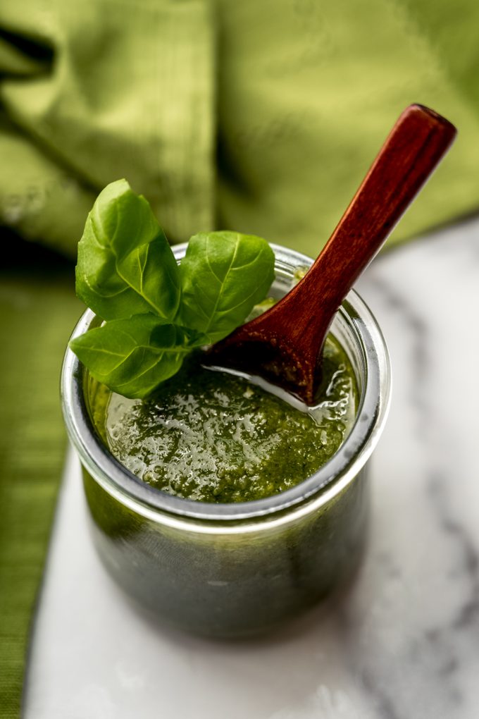 A jar of homemade pesto with a small wooden spoon in it.